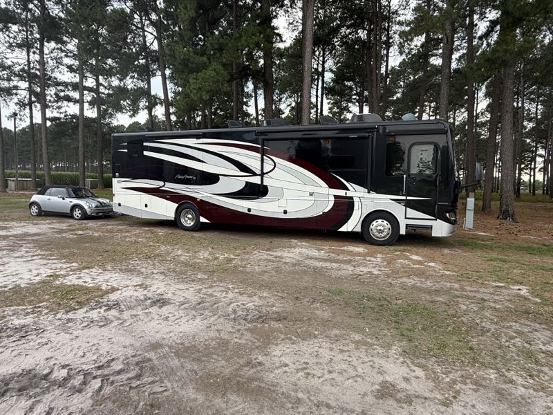 A Pace Arrow motorhome with a Mini Cooper toad under the pines